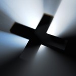 A cross with a light illuminating it from behind in the dark